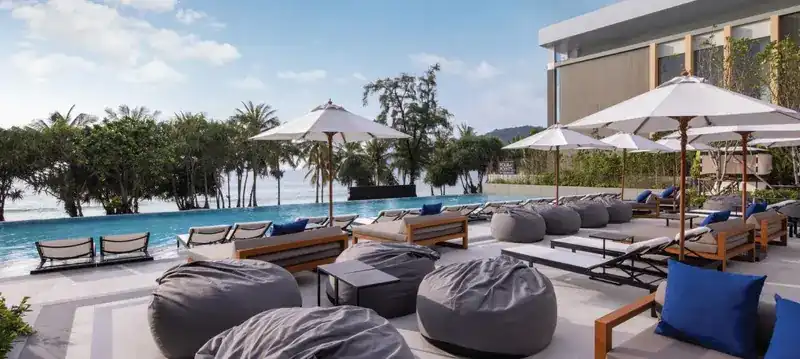 Pool deck with bean bags, loungers and parasols, palm trees and the sea beyond