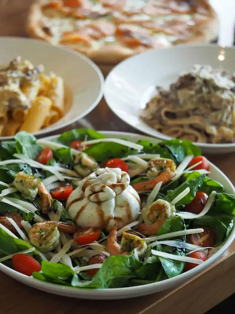 A salad with a whole fresh cheese, prawns, cherry tomatoes and shaved cheese