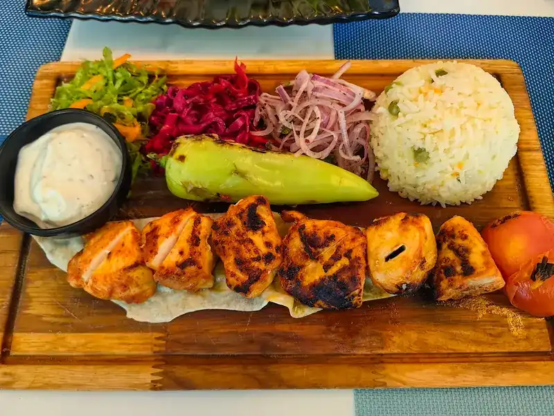 Chicken shish on a wooden board with rice, pickled onion, salad and yogurt
