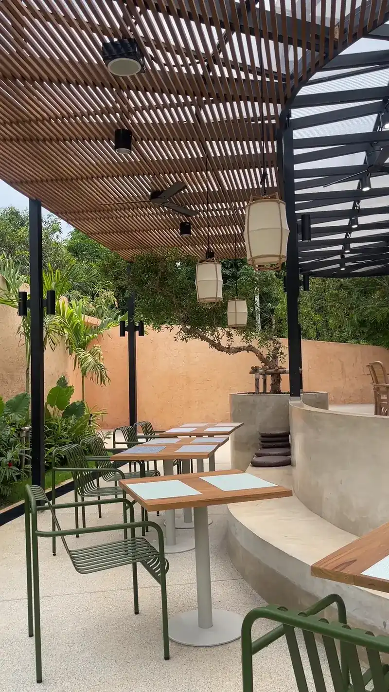 The terrace under a steel pergola, with green chairs and a clay-coloured wall