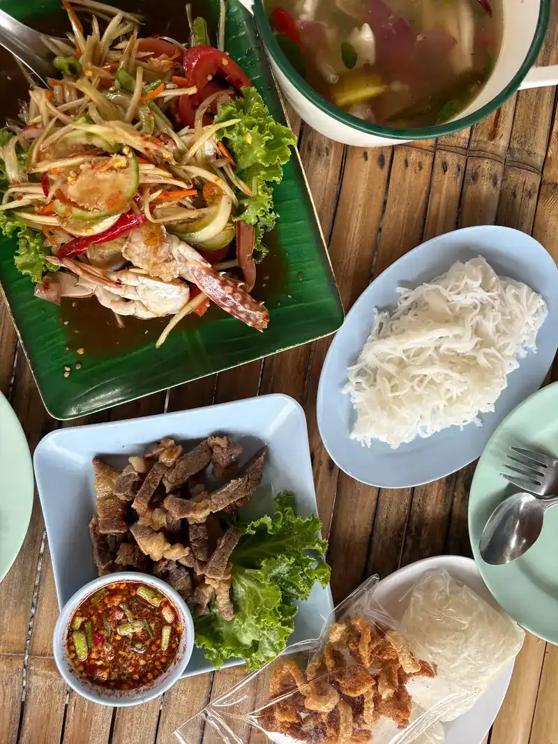 A spread of papaya salad, grilled meat with dipping sauce, rice noodles, pork crackling and soup