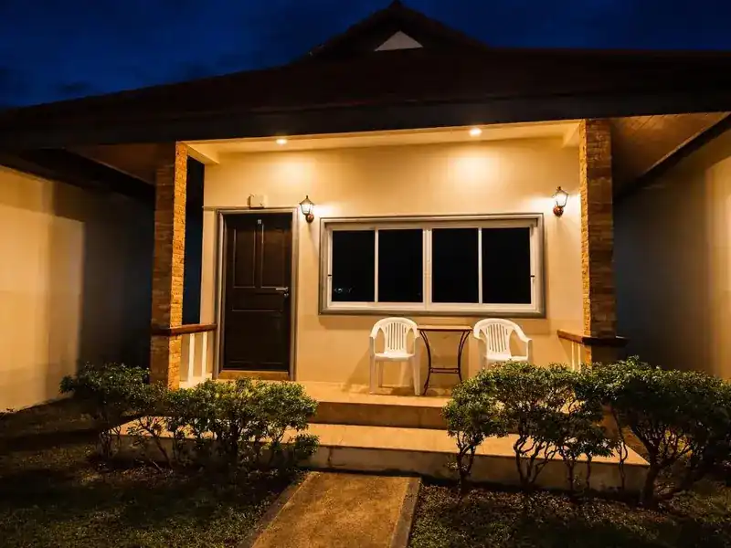 A bungalow porch with two chairs, lit at night