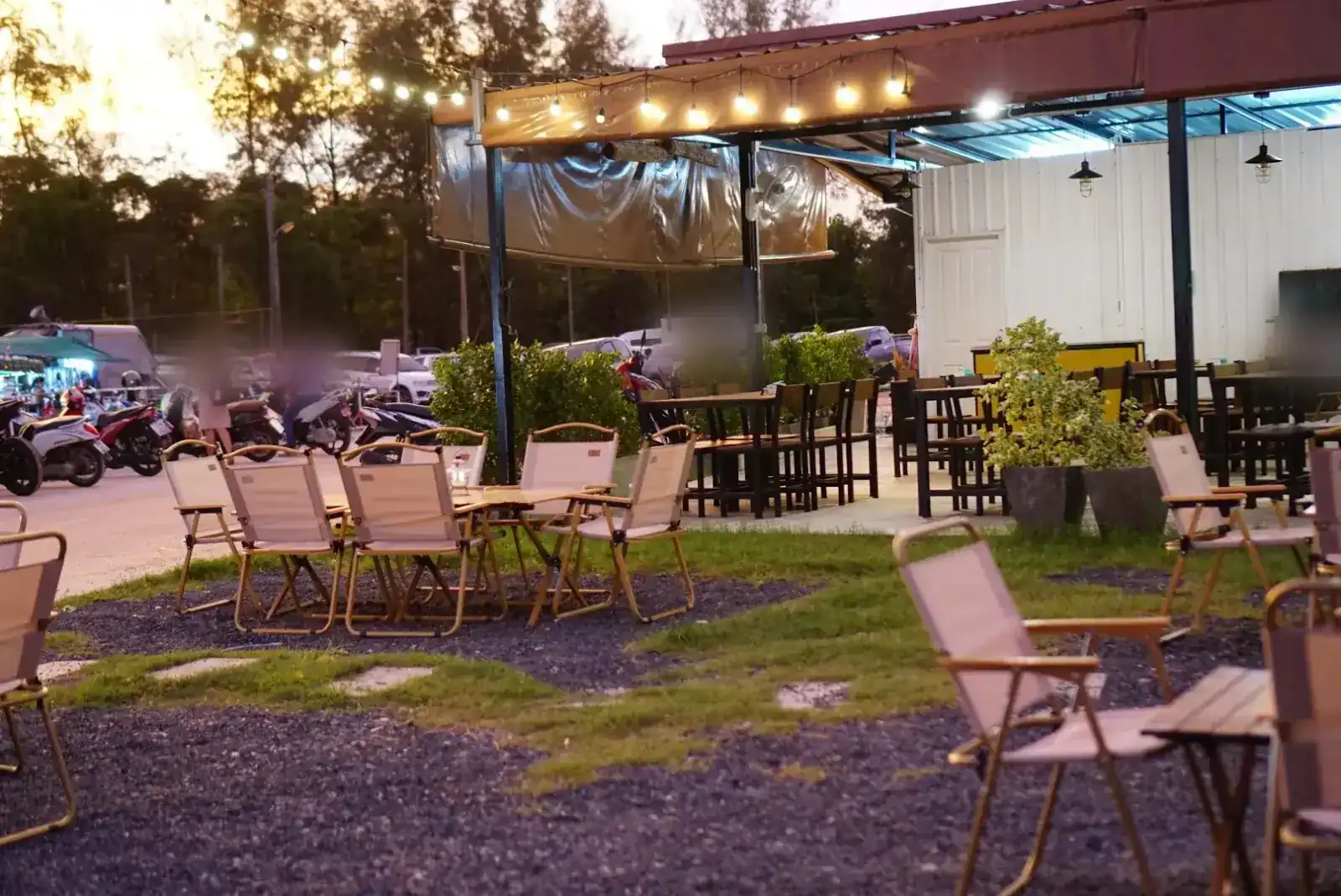 Ma Craft's garden at dusk: folding camp chairs on gravel and grass, string lights along a covered terrace.