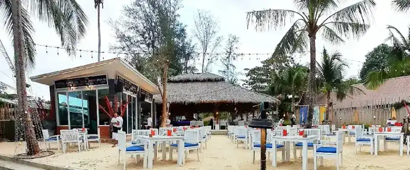 Coco Beach by day: white tables on the sand among the palm trees