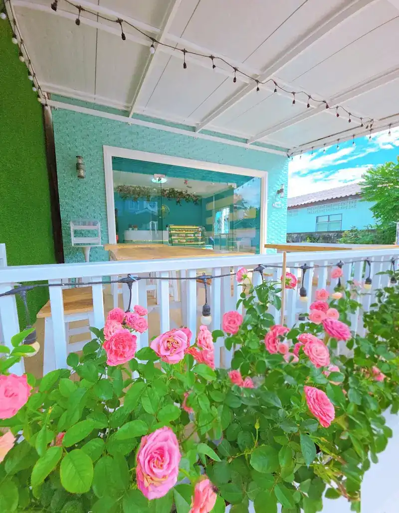 Pink roses along the white rail of the veranda, wooden tables under string lights, and the glass front of the shop