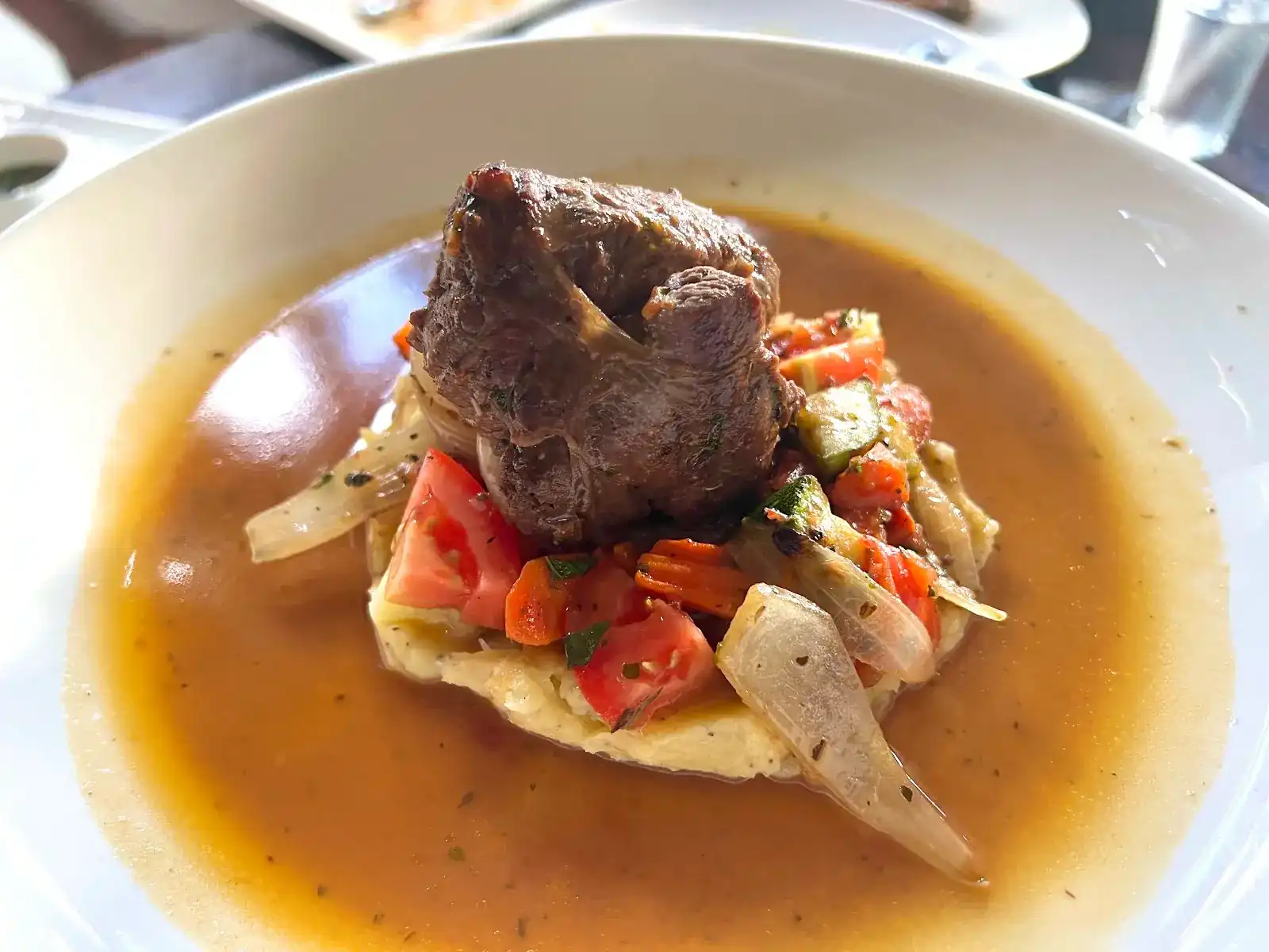 Braised meat on mashed potato with tomato, carrot, courgette and onion in its gravy