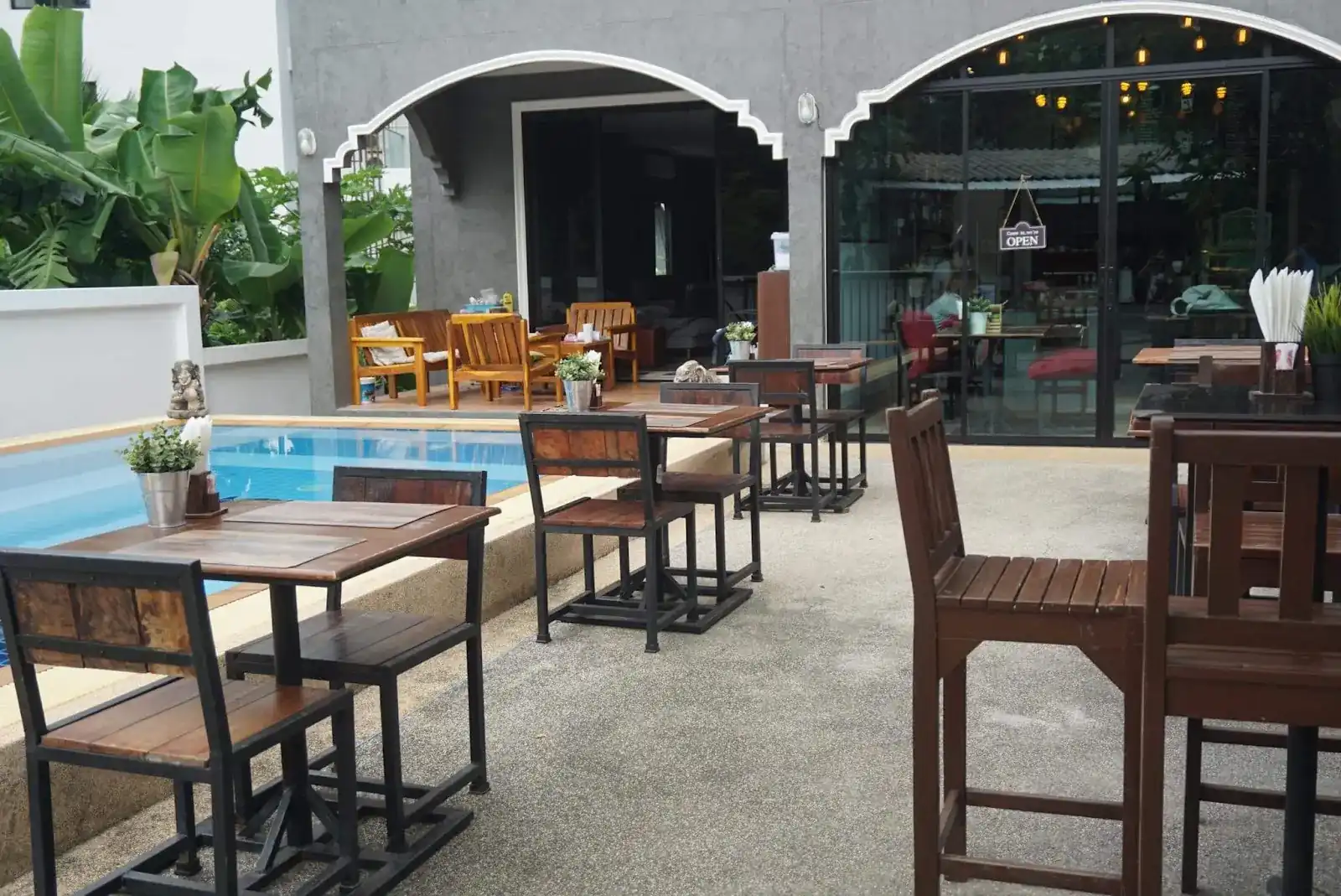 Wooden tables on the terrace beside the pool, in front of the house's glass doors