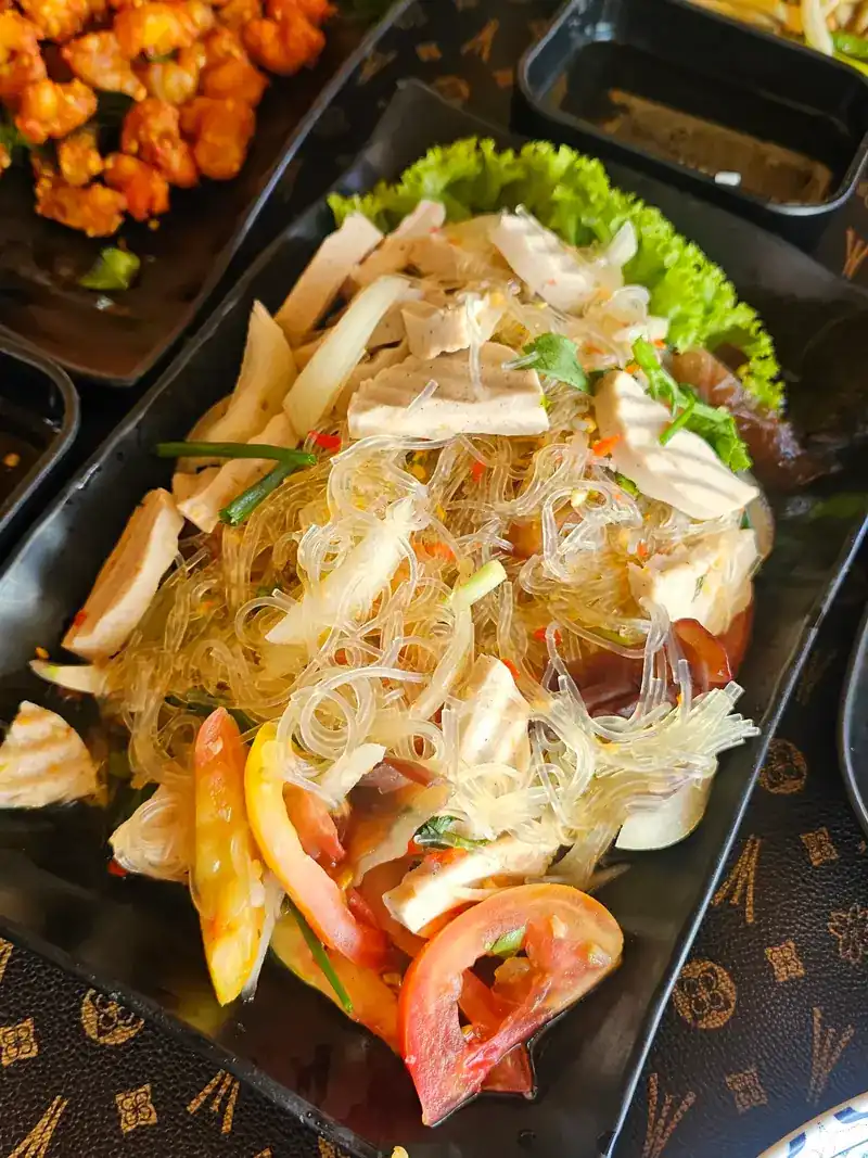 Glass noodle salad with squid, tomato and onion on a black plate