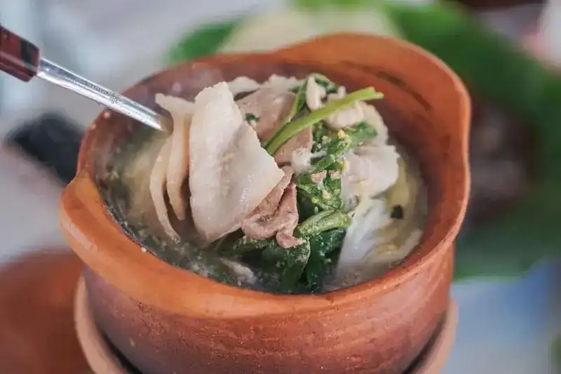 A clay pot of clear soup with sliced meat and greens