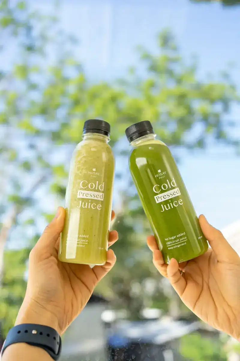 Two bottles of cold-pressed juice held up against the sky