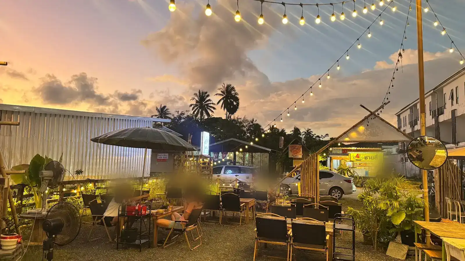 The open-air yard at dusk under strings of lights, with camp chairs and wooden tables