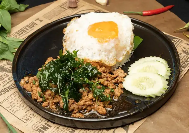 Pad krapow with a fried egg, rice and cucumber on a dark plate