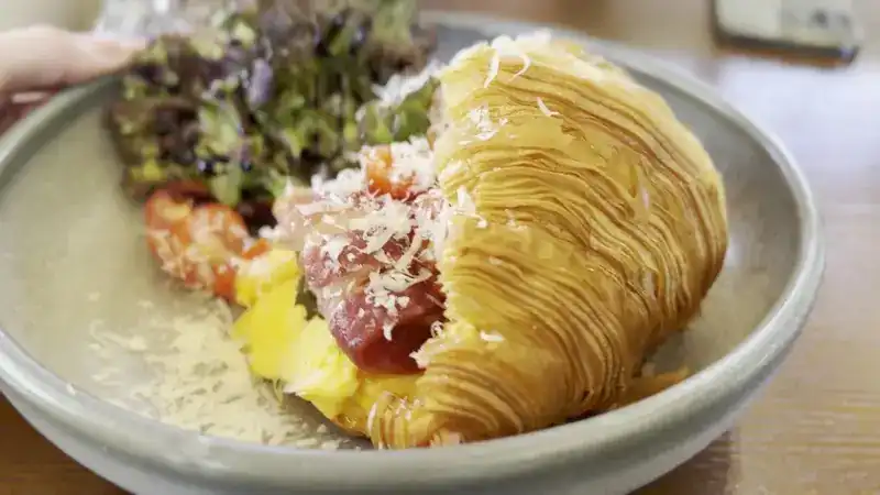 A crisp croissant with salad, egg and grated cheese
