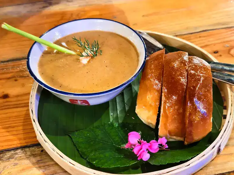 A bowl of soup with sliced toasted bread on a banana leaf in a bamboo tray