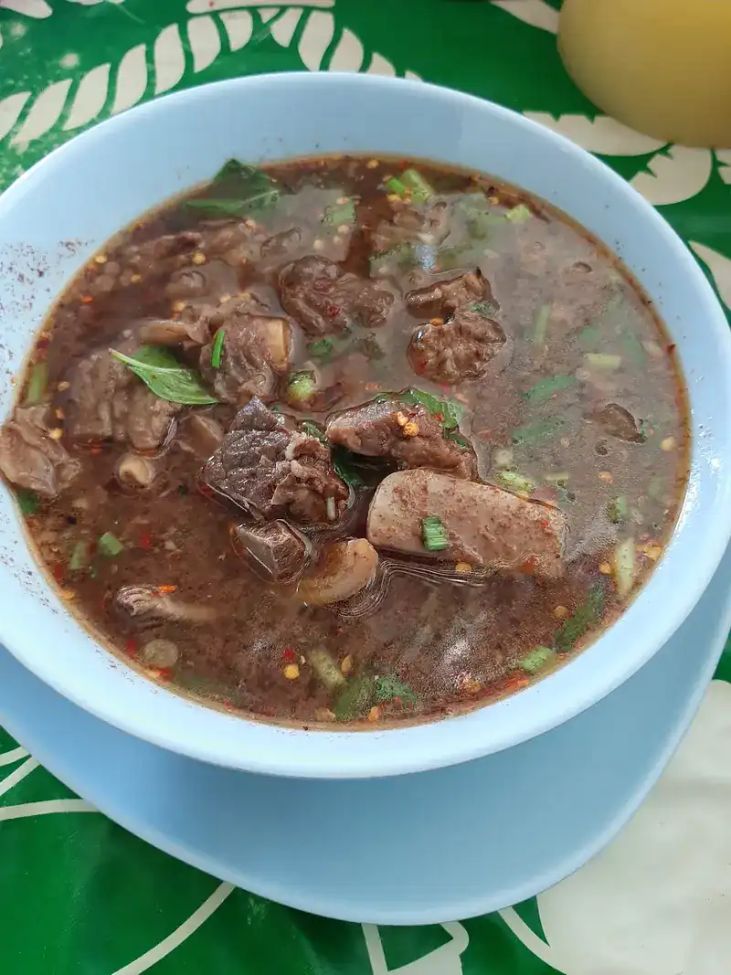 Beef in a dark, spicy broth with herbs in a pale blue bowl