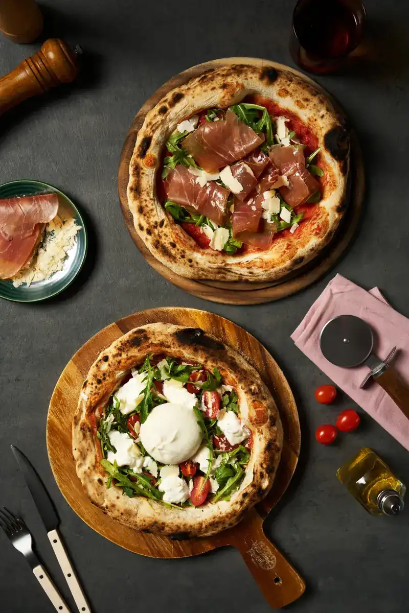 Two Neapolitan pizzas seen from above, one with Parma ham and one with burrata and rocket