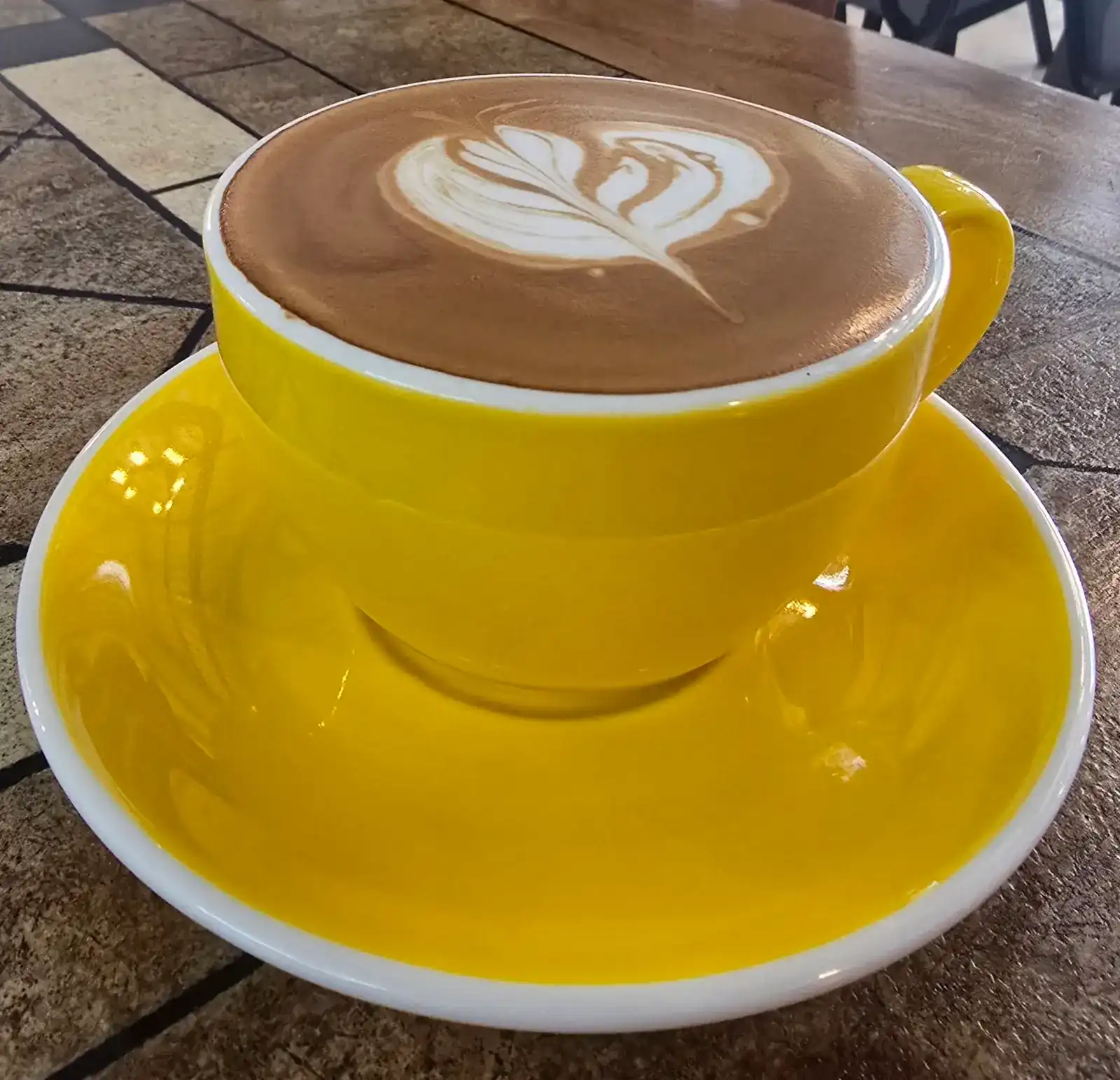 Latte with leaf art in a bright yellow cup and saucer