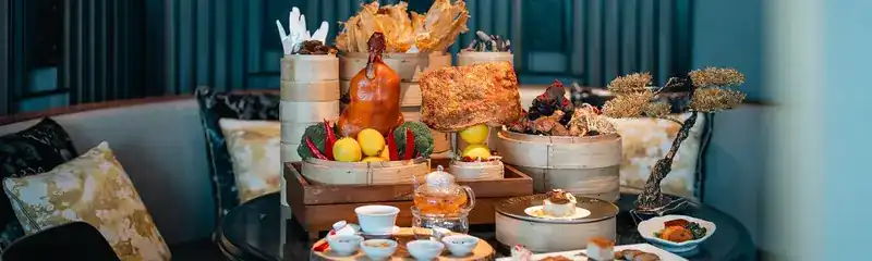 Roast duck, crispy pork and bamboo steamers set out on a table with tea
