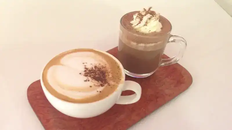 A coffee with latte art and a hot chocolate topped with whipped cream on a wooden tray