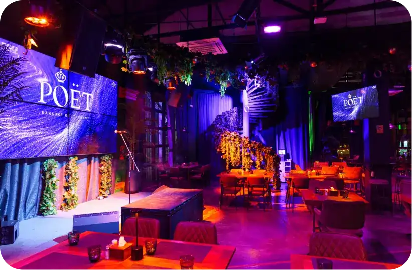 The stage at Poët: a wall of screens, a microphone stand and tables under violet light