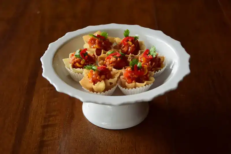 Small crisp pastry cups, filled and topped with chilli and coriander, on a white footed dish