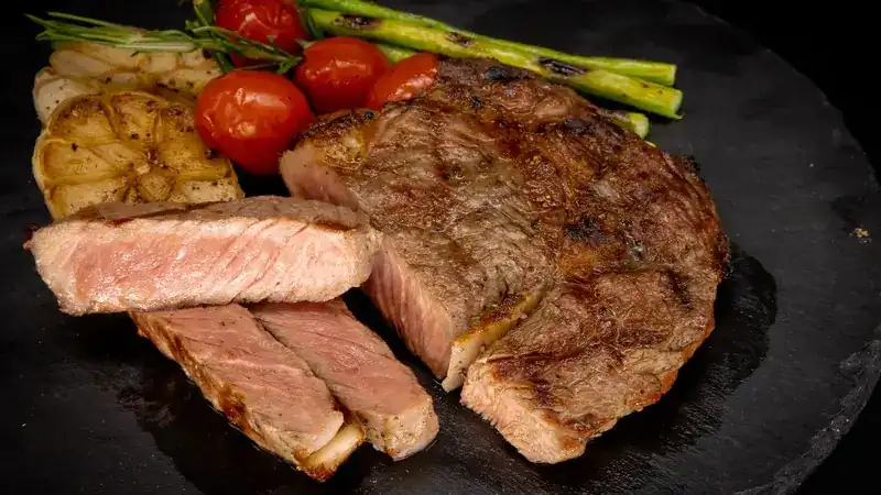 Sliced grilled beef on a slate with roast garlic, tomatoes and asparagus