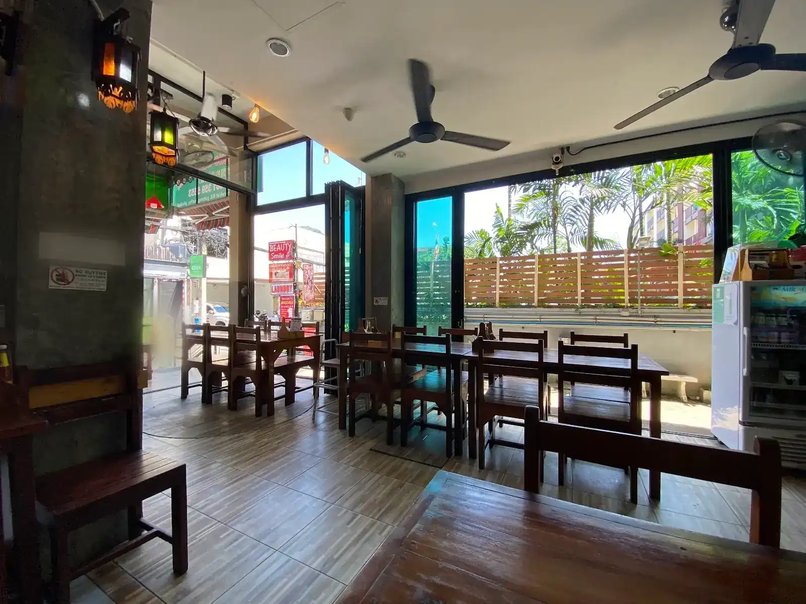 The dining room at Thai Smile: wooden tables, ceiling fans and glass doors folded open to the palms outside