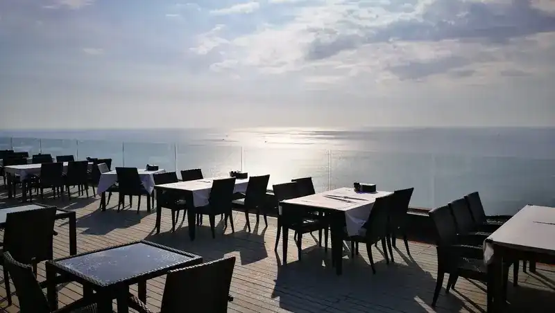The deck in the late afternoon, tables along the glass rail above the sea / ระเบียงยามบ่ายแก่ โต๊ะเรียงริมราวกระจกเหนือทะเล