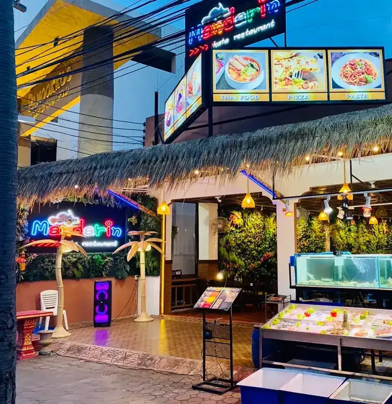 The restaurant at dusk: neon Mandarin sign, thatched roof, the ice table and a tank out front
