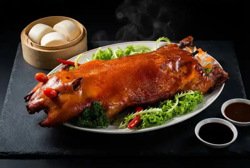 Whole barbecued suckling pig on a platter with steamed buns and dipping sauces