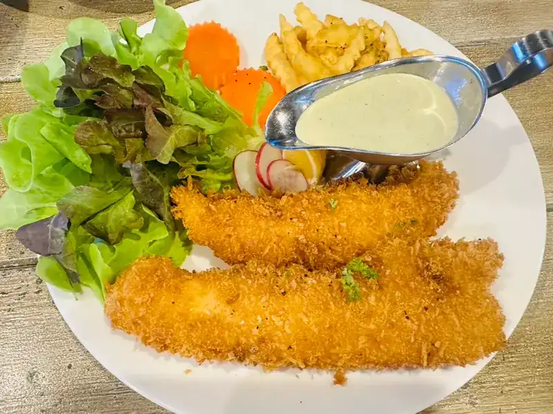 Two breaded fillets with fries, salad, carrot and a creamy sauce in a jug