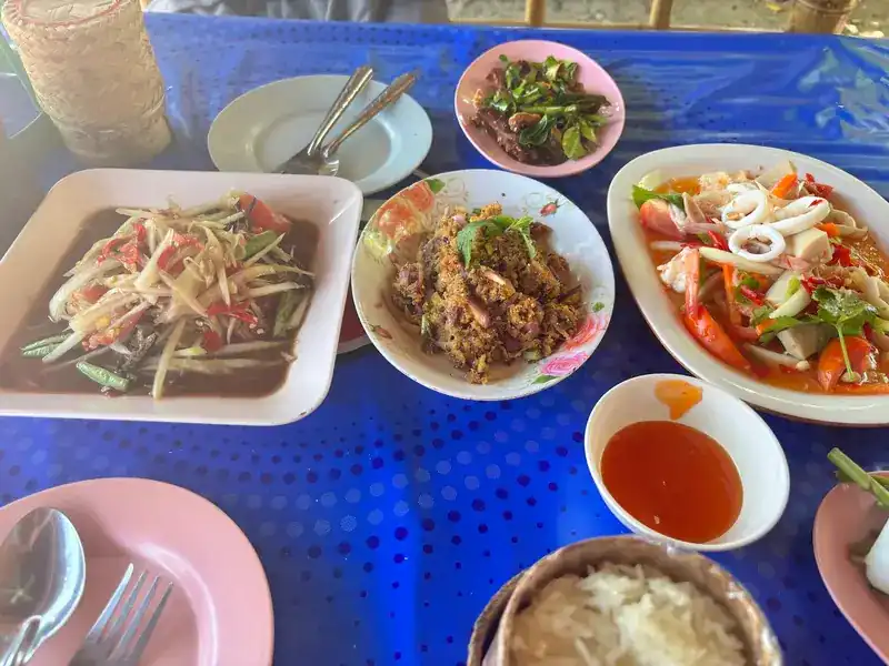 Papaya salad, larb and a squid salad on a blue tablecloth, with chilli sauce and rice