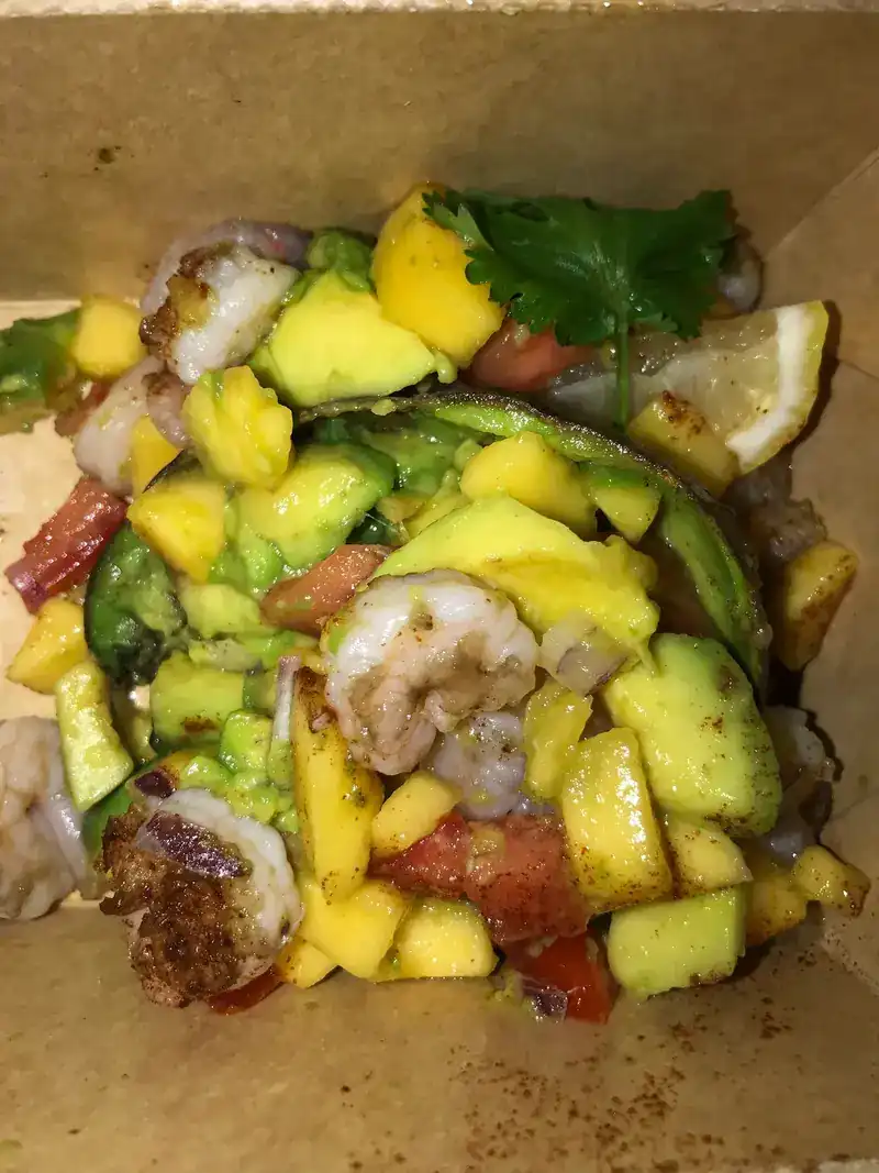 Grilled avocado with mango, shrimp and tomato in a takeaway box