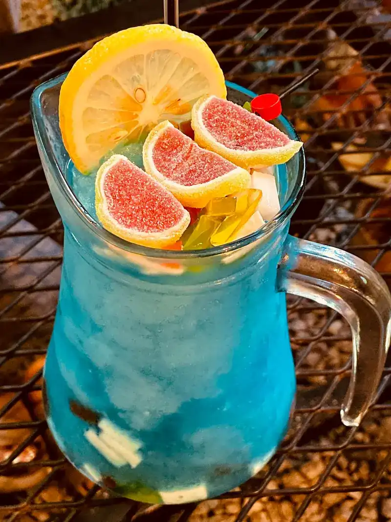 A blue iced drink in a glass jug, topped with lemon and fruit jellies