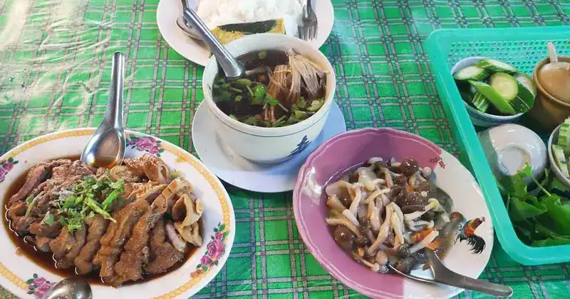 A plate of stewed pork leg with a bowl of soup and fresh vegetables on the side
