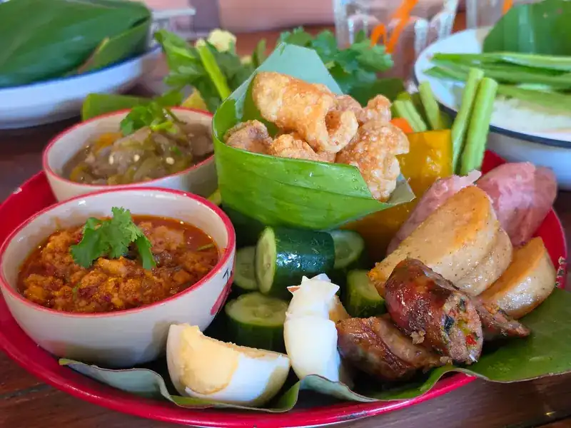 A northern platter on a red tray: grilled sausage, pork crackling, two chilli dips, vegetables and boiled egg