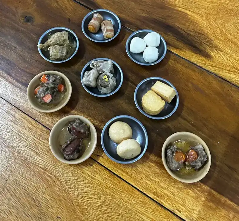 Nine small saucers of dim sum on a wooden table