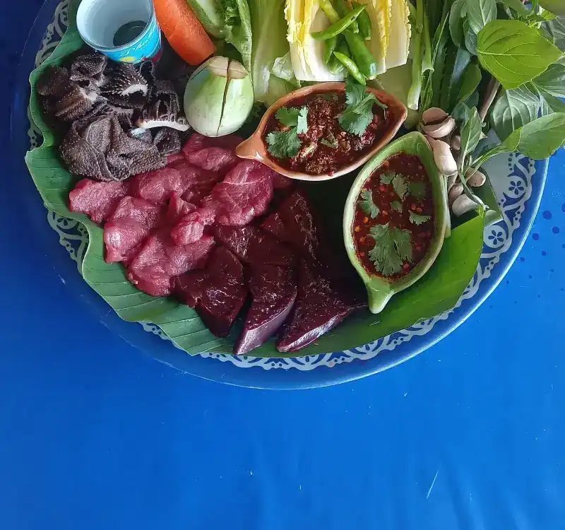 Sliced raw beef and tripe on banana leaf, with fresh herbs, vegetables and two chilli dips