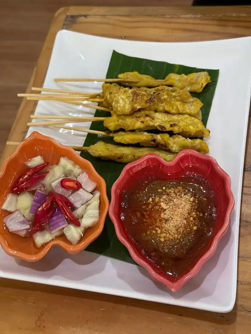 Pork satay on a banana leaf with peanut sauce and cucumber relish