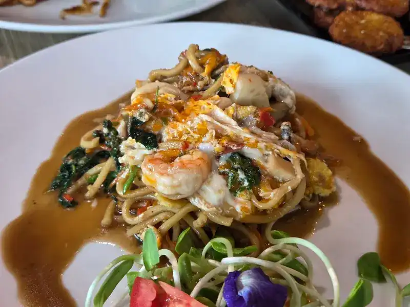 Spicy fried noodles with prawn and seafood, a fresh salad with a butterfly pea flower on the side