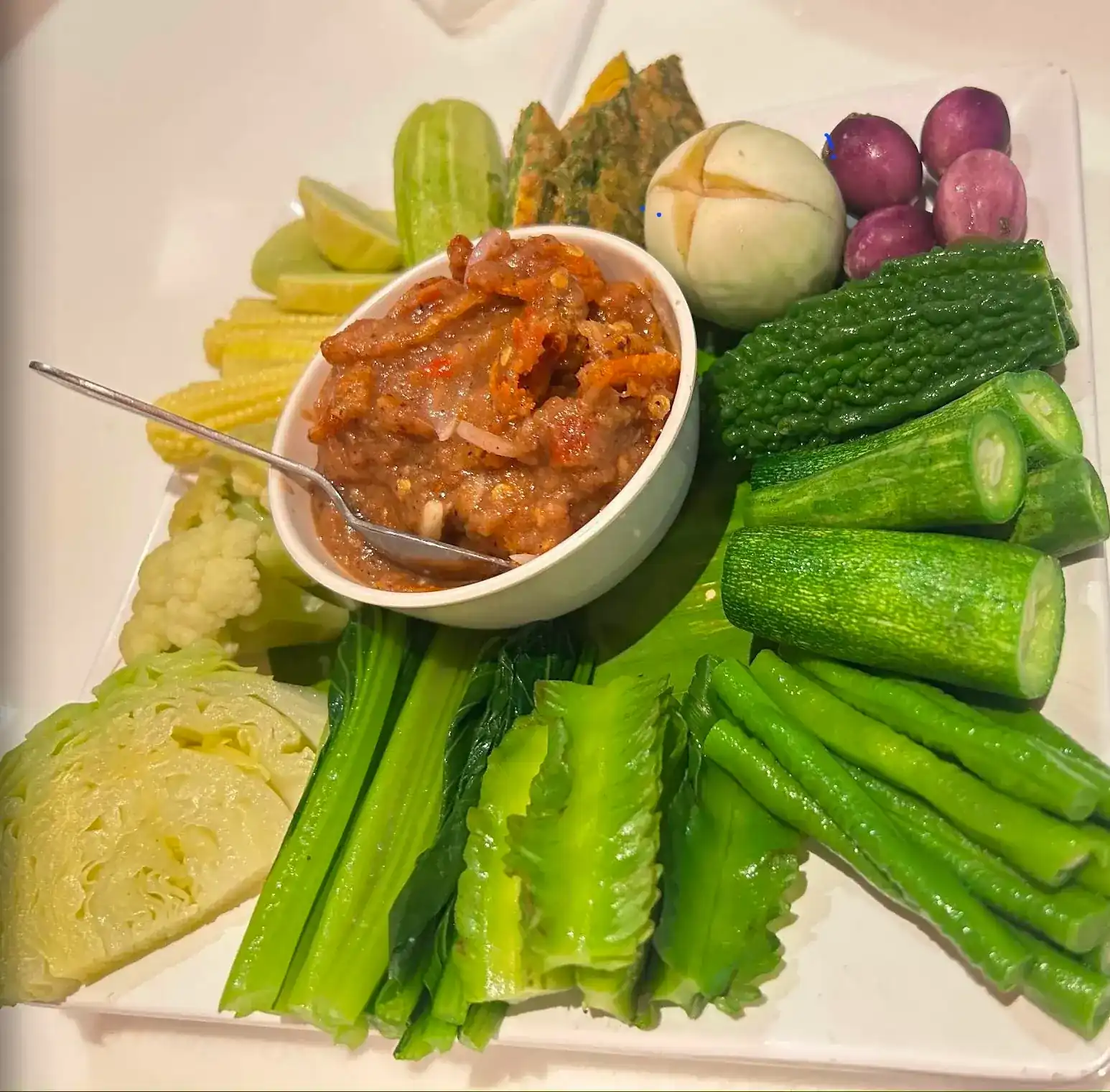 A bowl of nam phrik chilli dip with cucumber, long beans, bitter gourd, cabbage and other fresh vegetables