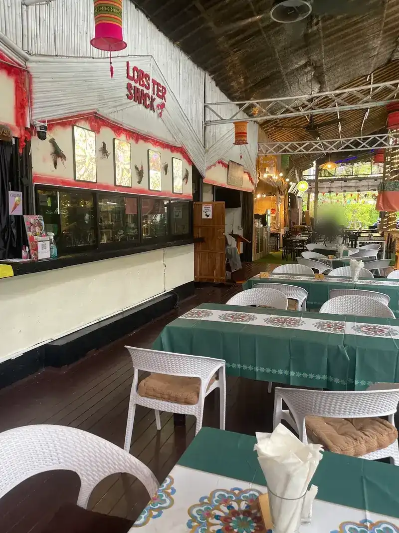 Inside Lobster Shack: green tablecloths, white chairs and the red sign on a white bamboo wall