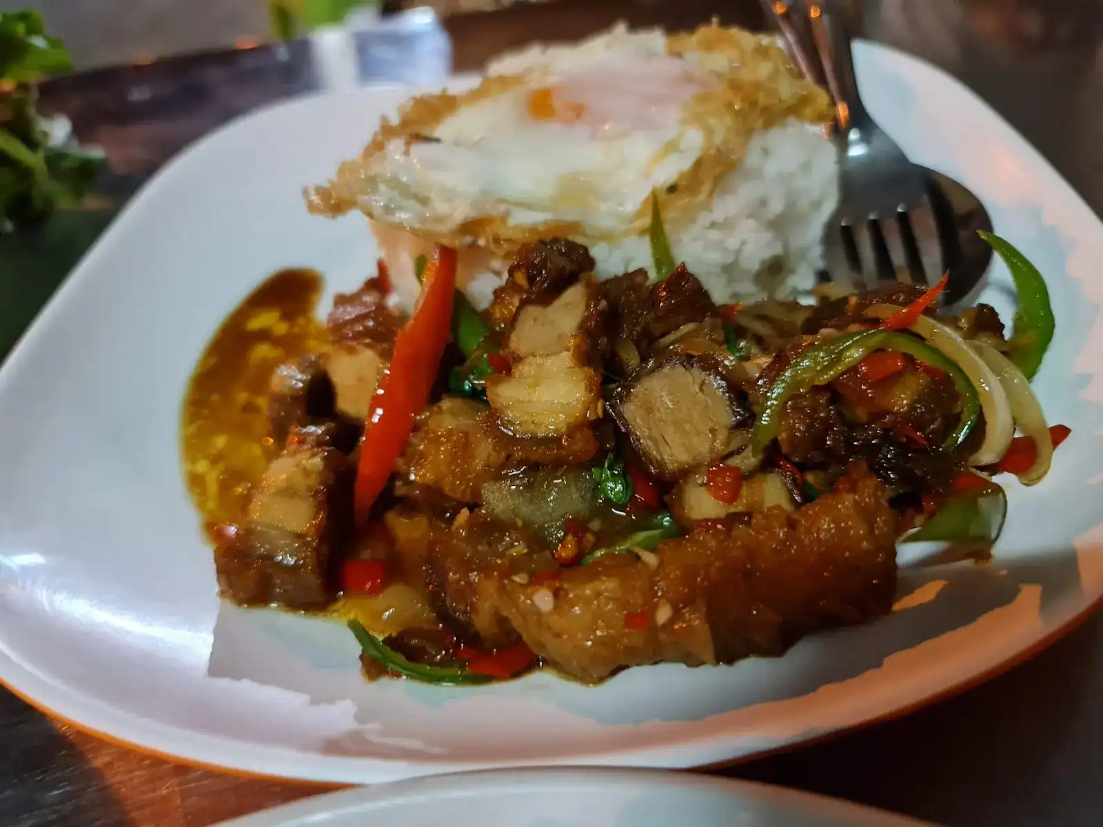 Crispy pork stir-fried with red and green chillies and onion, with rice and a fried egg on top