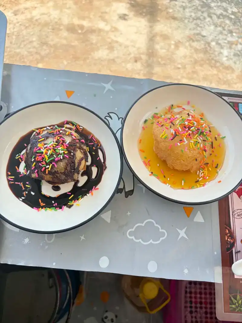 Two round desserts on white plates, one under dark chocolate sauce and one under a golden sauce, both with rainbow sprinkles