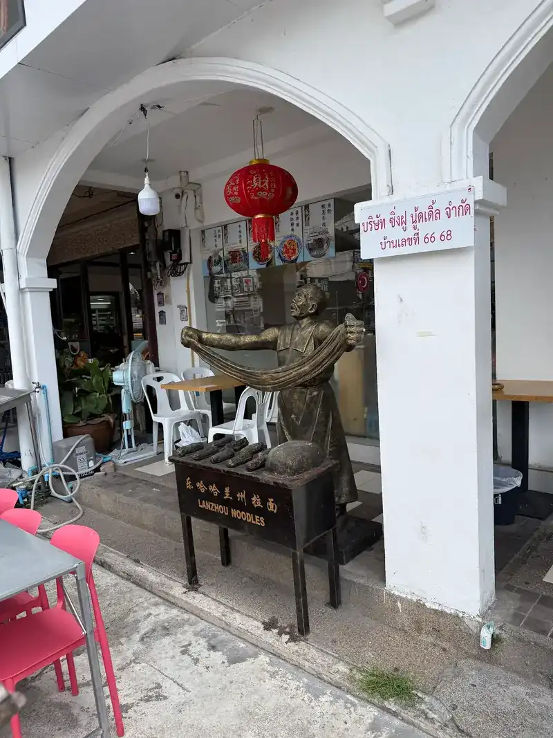Statue of a man pulling noodles at the front door, under white arches and a red lantern