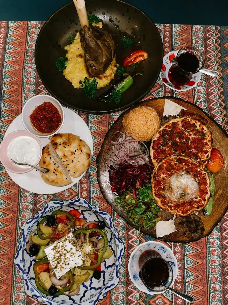 Thin Turkish flatbreads topped with minced meat, with bread, dips and salad on a patterned tablecloth