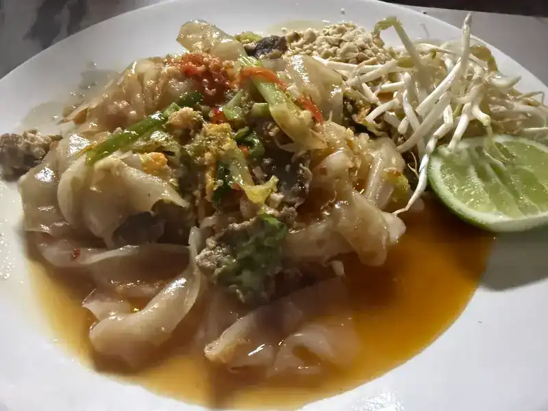 Wide rice noodles in a glossy sauce with bean sprouts, crushed peanuts and lime