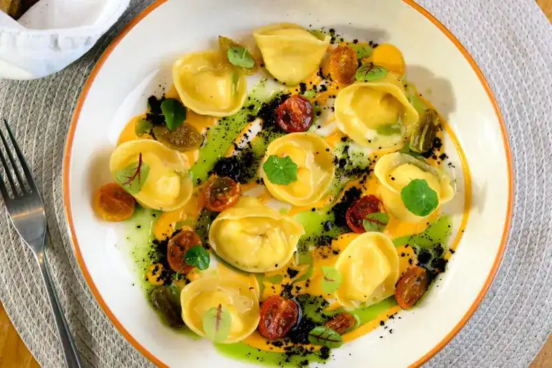 Hand-folded filled pasta with roasted tomatoes, herb oil and small leaves