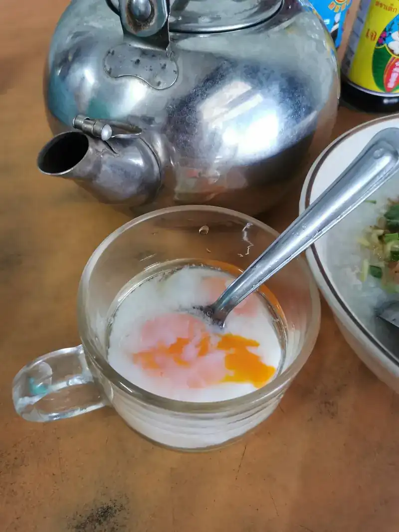A soft-boiled egg in a glass cup beside an aluminium kettle