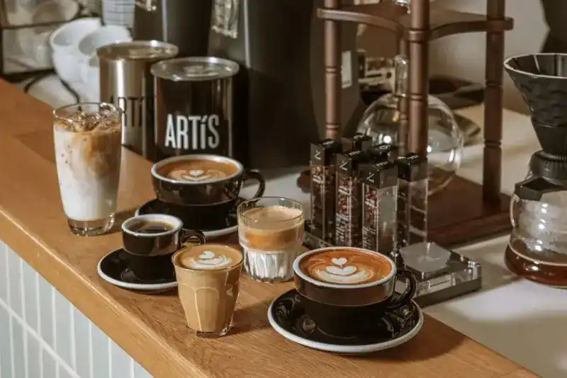 Flat whites, a cappuccino, espresso and an iced latte on the oak counter beside an ARTiS coffee tin